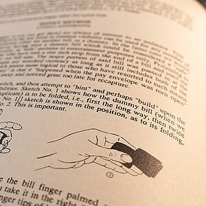 A person performing a magic trick with a coin and a small object, demonstrating sleight of hand.