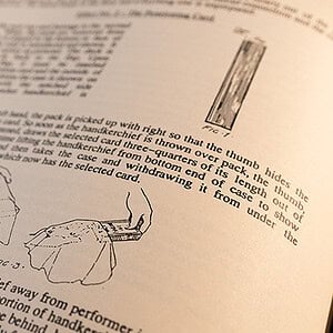 A person holding a magic trick instruction booklet with illustrations of a card trick.