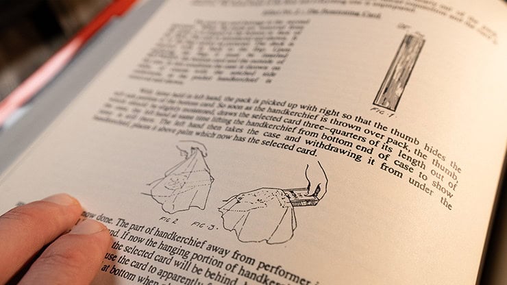 A person holding a magic trick instruction booklet with illustrations of a card trick.