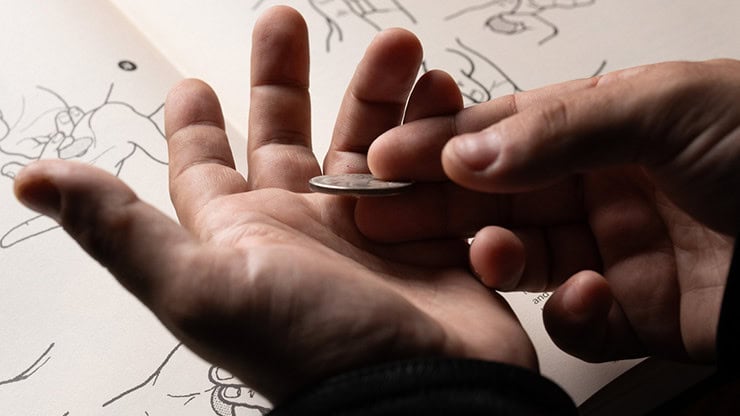 A person balancing a coin on their fingers over a sketchbook with drawings.
