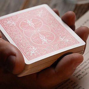A deck of playing cards held in a person's hand on a wooden surface.