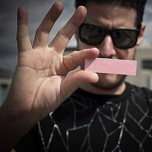 A magician performing a card trick with a pink card outdoors.