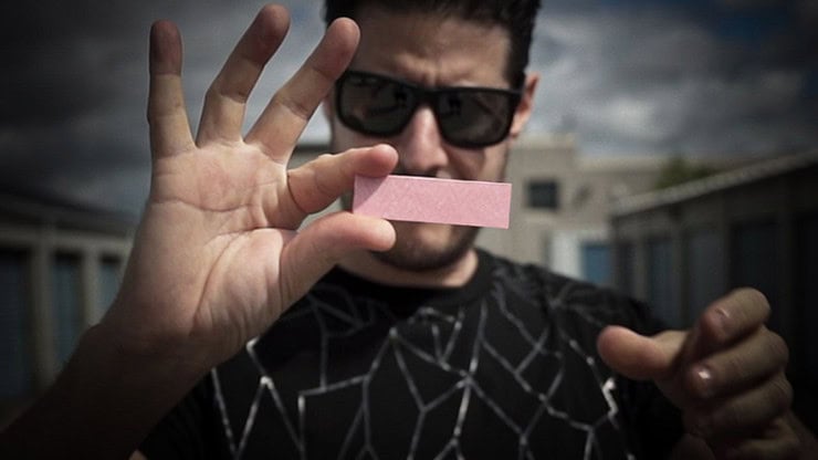 A magician performing a card trick with a pink card outdoors.