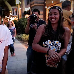 A young woman smiling and holding a bouquet of daisies at an outdoor event.