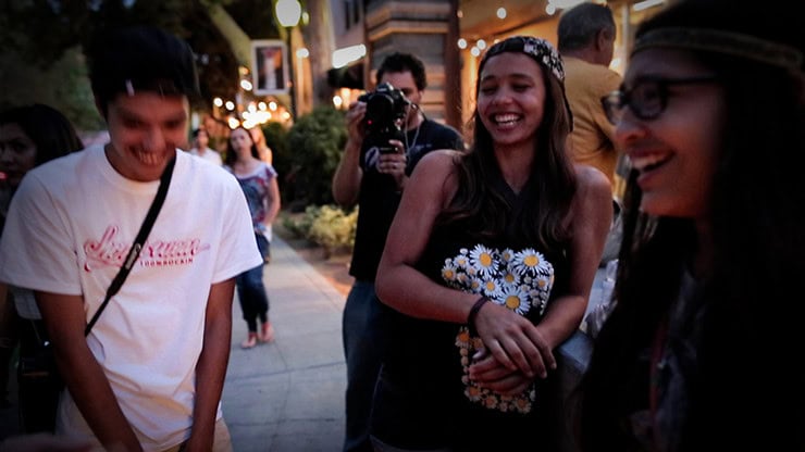 A young woman smiling and holding a bouquet of daisies at an outdoor event.