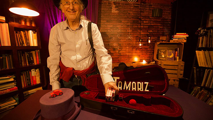 Juan Tamariz smiling behind a table with his TAMARIZ violin case holding a deck of cards, from the Magic From My Heart video collection