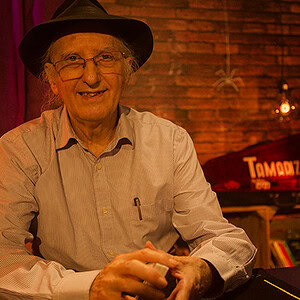 Juan Tamariz performing magic in a cozy, brick-walled shop setting.