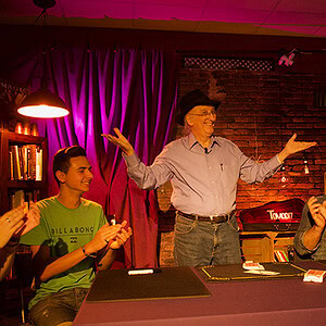 Magician performing card tricks for an audience in a cozy, dimly lit room.