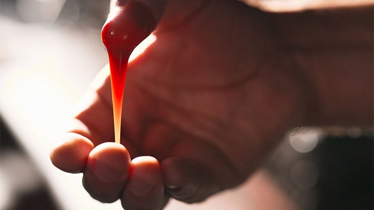 A colorful magic illusion with a red liquid drop falling from a magician’s hand.