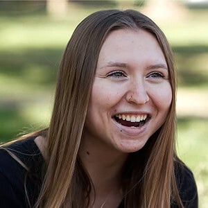 A smiling young woman enjoying a magic show outdoors in a park setting.