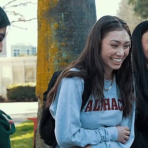 A woman laughing with two friends outdoors in a park setting.