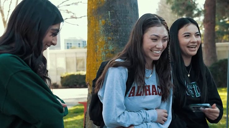 A woman laughing with two friends outdoors in a park setting.