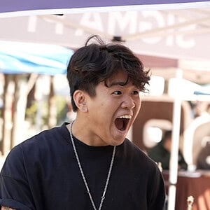 A lively outdoor event with two young men engaging in a joyful conversation under a tent.