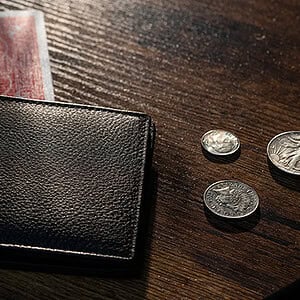 A wallet with cash and coins on a wooden surface.