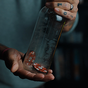 Close-up of a hand holding a glass bottle with dice inside, magic shop scene.
