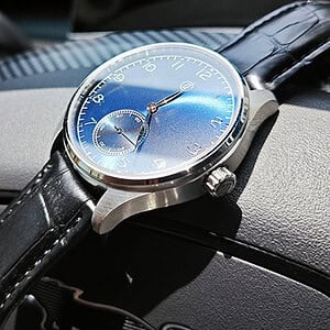 A sleek blue watch with a black leather strap resting on a car dashboard.