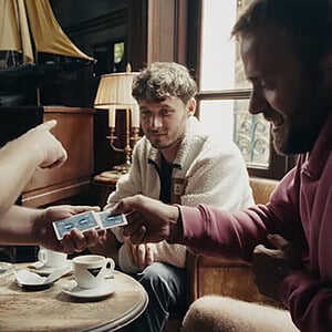 A man performing a card trick for two friends in a cozy cafe setting.