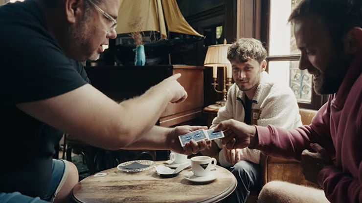 A man performing a card trick for two friends in a cozy cafe setting.