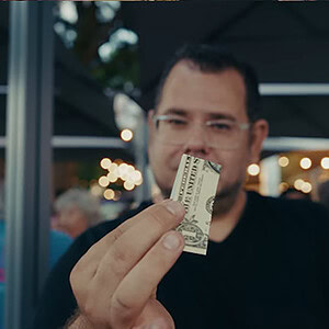 A man performing a magic trick with a dollar bill at an outdoor event.