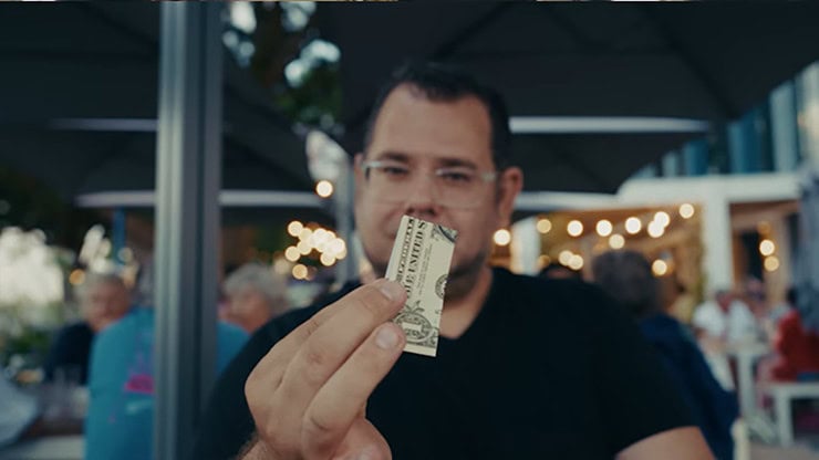 A man performing a magic trick with a dollar bill at an outdoor event.