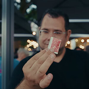 A man performing a card trick at an outdoor event with string lights in the background.