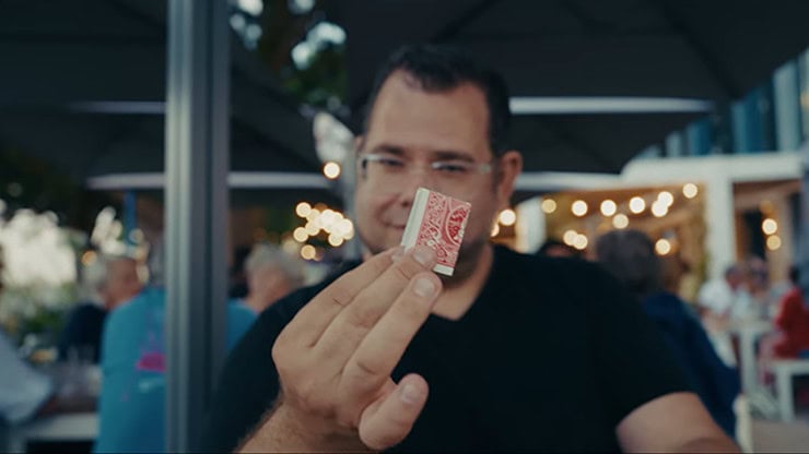 A man performing a card trick at an outdoor event with string lights in the background.