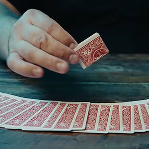 A magician performing card tricks with a deck of playing cards on a wooden table.