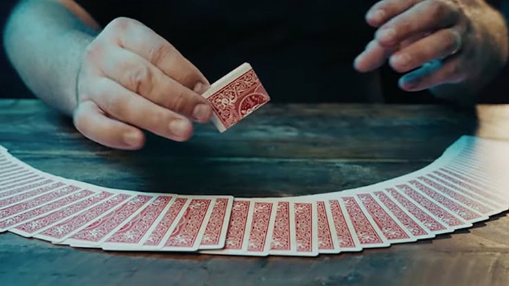 A magician performing card tricks with a deck of playing cards on a wooden table.