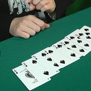 A colorful arrangement of playing cards in a fan shape on a green table, with a person's hand reachi.