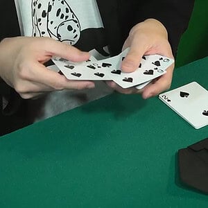 A person performing a card trick with playing cards on a green table, showcasing magic and illusion.
