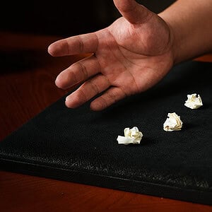 Close-up of a magician's hand performing a magic trick with small paper balls on a black mat.
