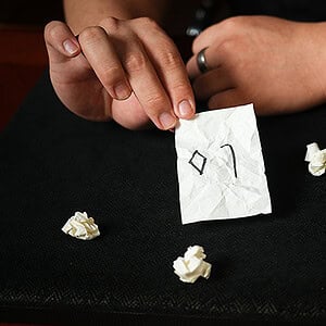 Close-up of a hand holding a small paper with a magic symbol, surrounded by crumpled paper pieces.