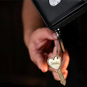 Close-up of a hand holding a black wallet with a gold key charm reading 'Smile'.
