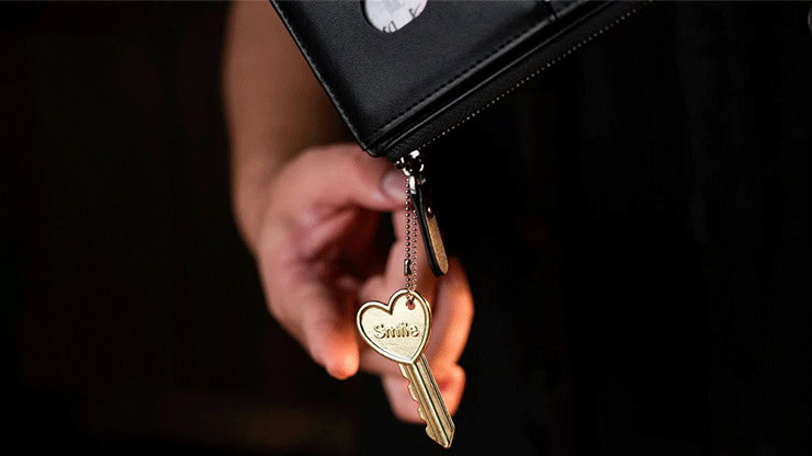 Close-up of a hand holding a black wallet with a gold key charm reading 'Smile'.