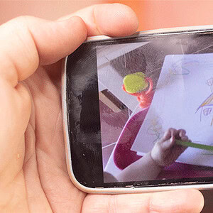 Child drawing a colorful house on paper with a green crayon.