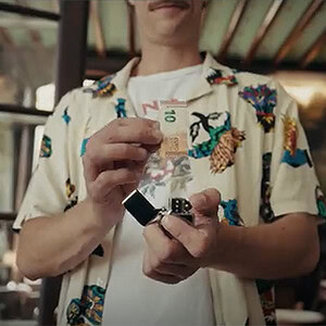 A person holding a small black device, with a colorful patterned shirt, in a cozy indoor setting.