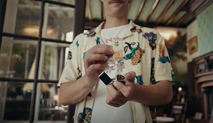 A person holding a small black device, with a colorful patterned shirt, in a cozy indoor setting.