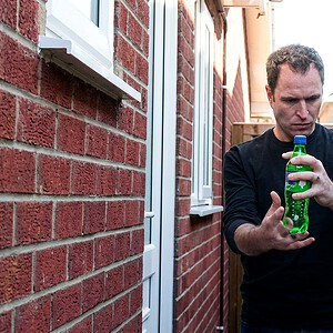 reKap by Richard Griffin magic trick - performer demonstrating the vanishing bottle cap with a green soda bottle