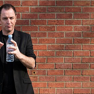reKap by Richard Griffin magic trick - performer demonstrating the bottle cap effect with a water bottle against a brick wall