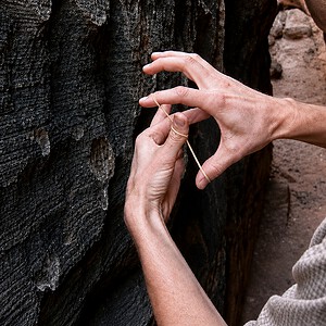 Rubber Band Penetration close-up — hands stretching the band against a slot canyon rock wall